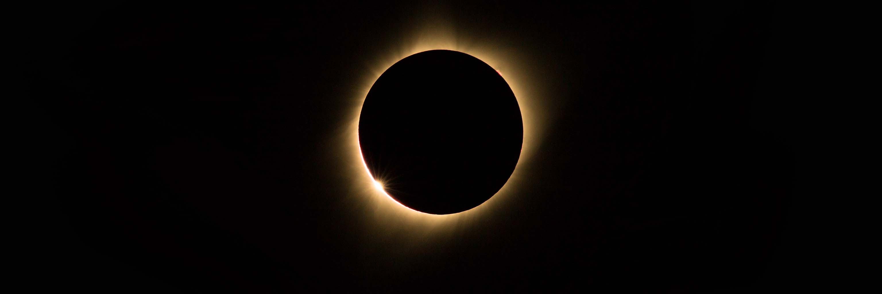 During the 2017 solar eclipse, the moon appeared as a dark circle over the sun. Light from the sun escaped from behind the moon, forming a thin circle of light around the moon. The sky behind is black.