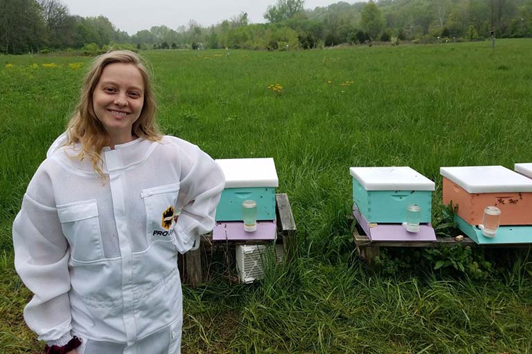 Audrey Parish poses for a picture next to a row of beehives.