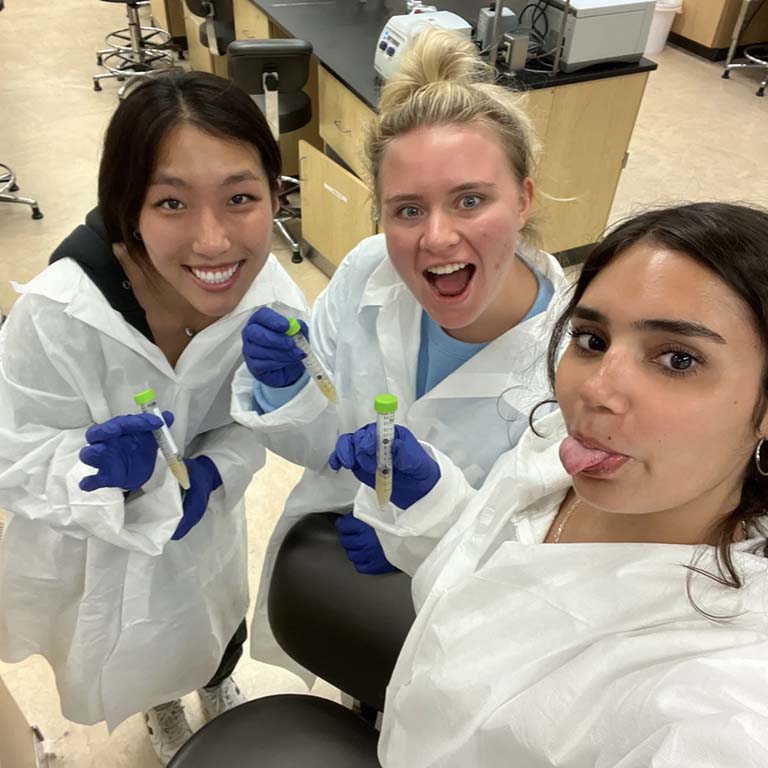 Danielle Vance sticks out her tongue as she poses with two of her lab mates for a photo.