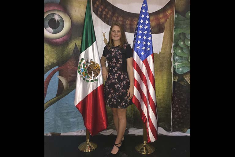Fulbright Scholar Madeline Danforth stands between the Mexican and U.S. flags in Mexico City at the “museo de arte popular” at an event for her program.
