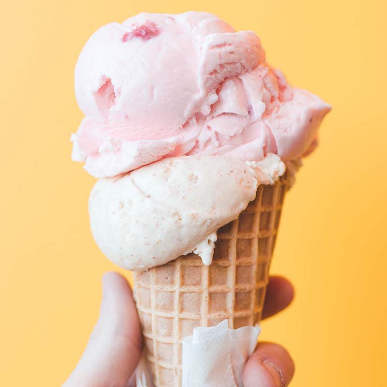 A dip of strawberry ice cream on a sugar cone.
