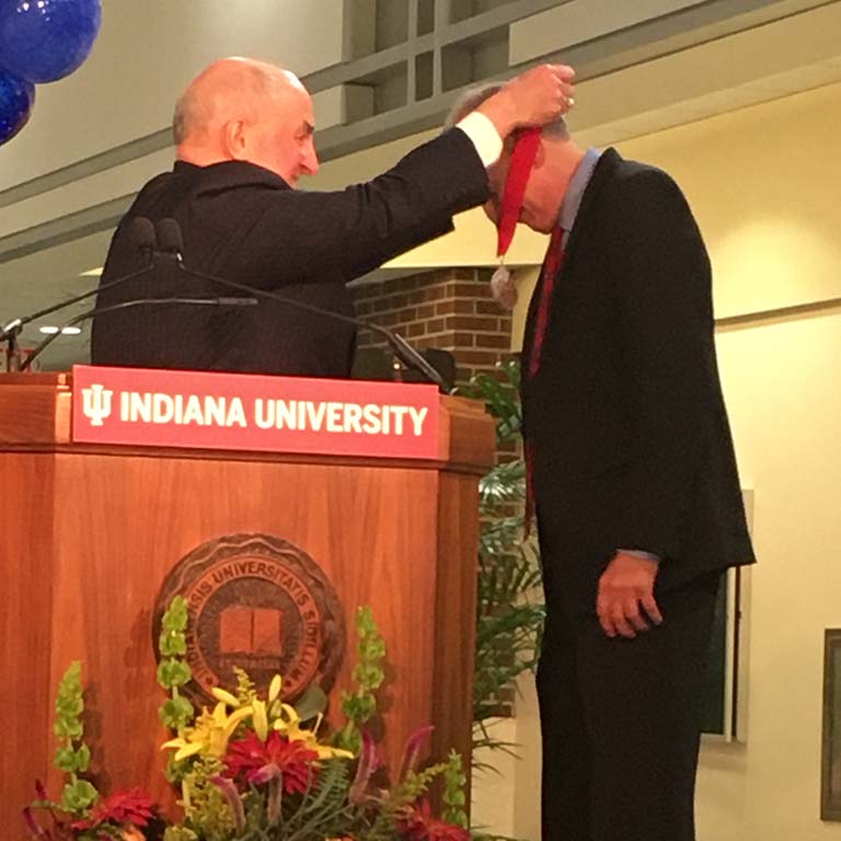 IU President McRobbie places the red ribbon holding the silver medal over Jeff Palmer's head as he presents Palmer with the IU President's Medal for Excellence.