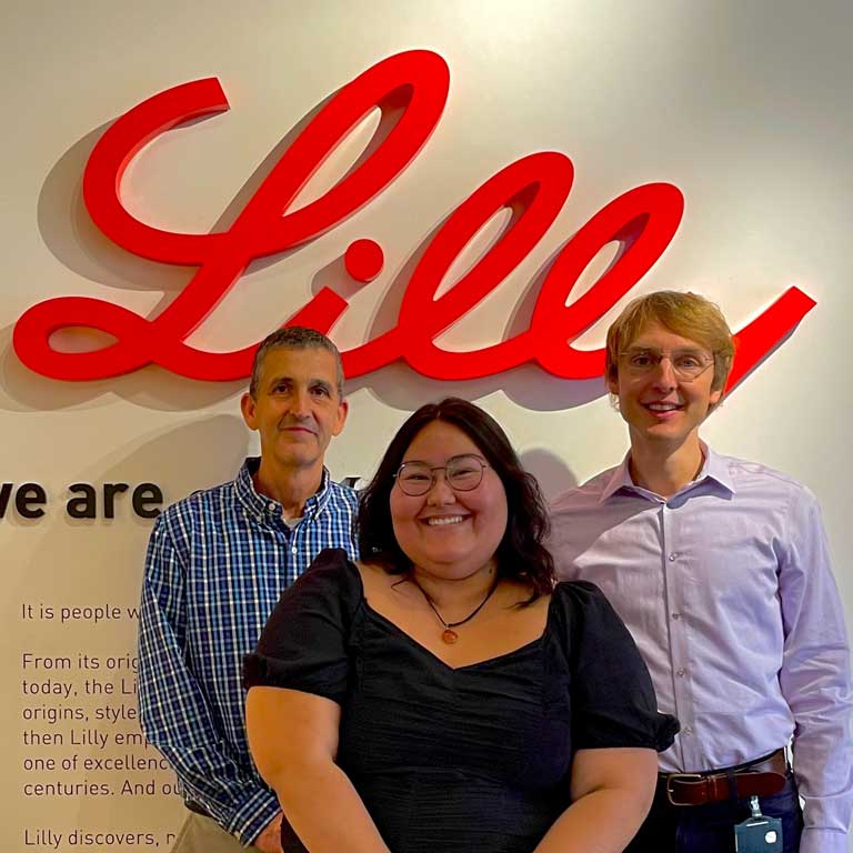 Lauren 'Wren' Garcia (center) poses in front of an Eli Lilly Company sign with technical mentors Richard T. Pickard and Henning Stockmann.
