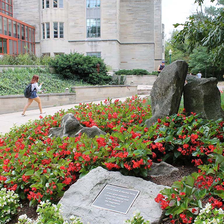 Students walking by Jordan Hall on IU Bloomington campus. A bed of red begonias in the foreground.
