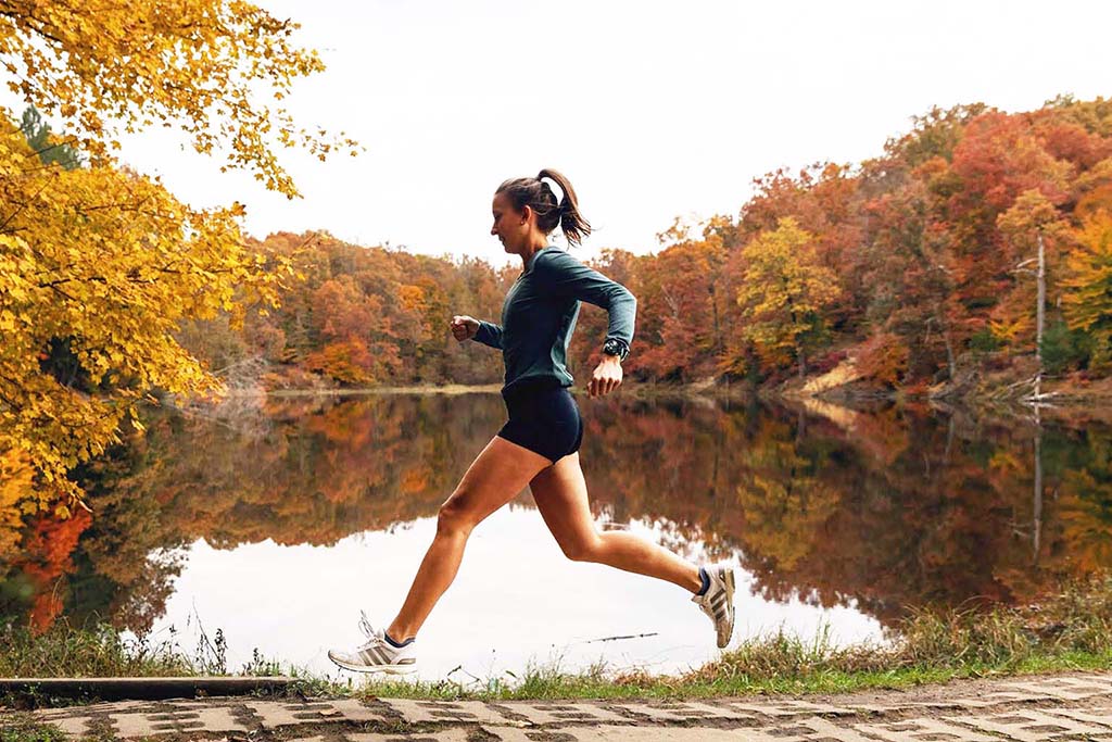 Olivia Ballew running near a lake in Brown County State Park. The tree leaves are in fall colors of yellow, orange, and red.