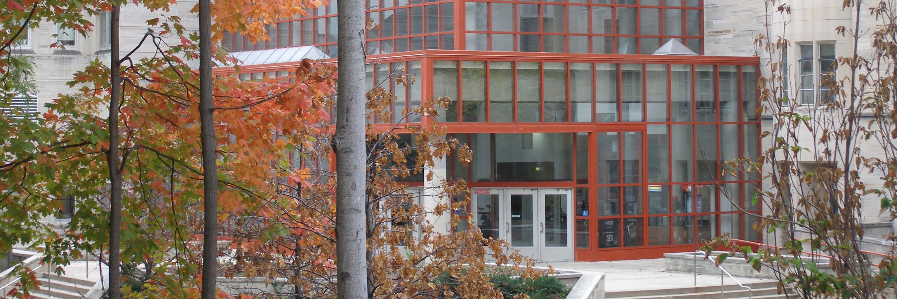 Looking through orange, red, and green autumn leaves toward the atrium entrance at the northwest corner of the Biology Bldg. on the Indiana University Bloomington campus.