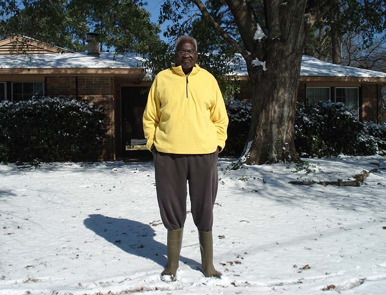 Nathan Okia stands in front of his home in Montgomery, Alabama, in 2018, after snow blanketed the ground and rooftops. Green leaves can be seen on the trees.