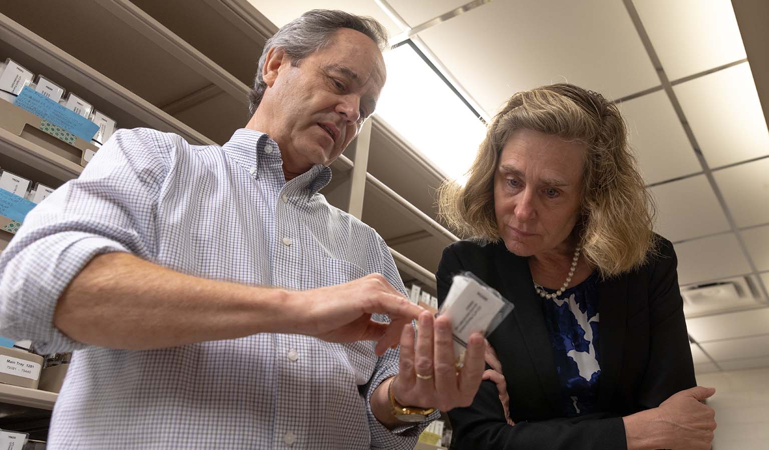 Kevin Cook (left) points at the label on a vial of one of the living fly cultures while talking with Pamela Whitten.