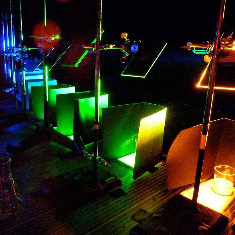 Mirrors are used to reflect different colors of light onto beakers with samples of the ocean bacterium Synechococcus.